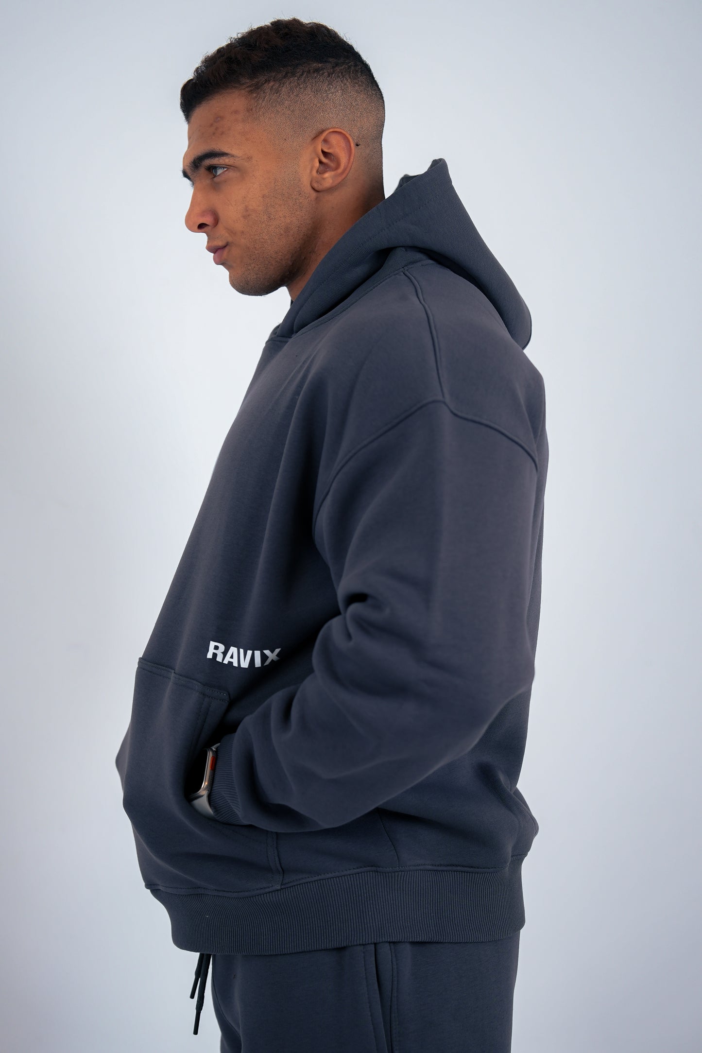 Man wearing a dark gray hoodie with 'RAVEX' branding on a light gray background