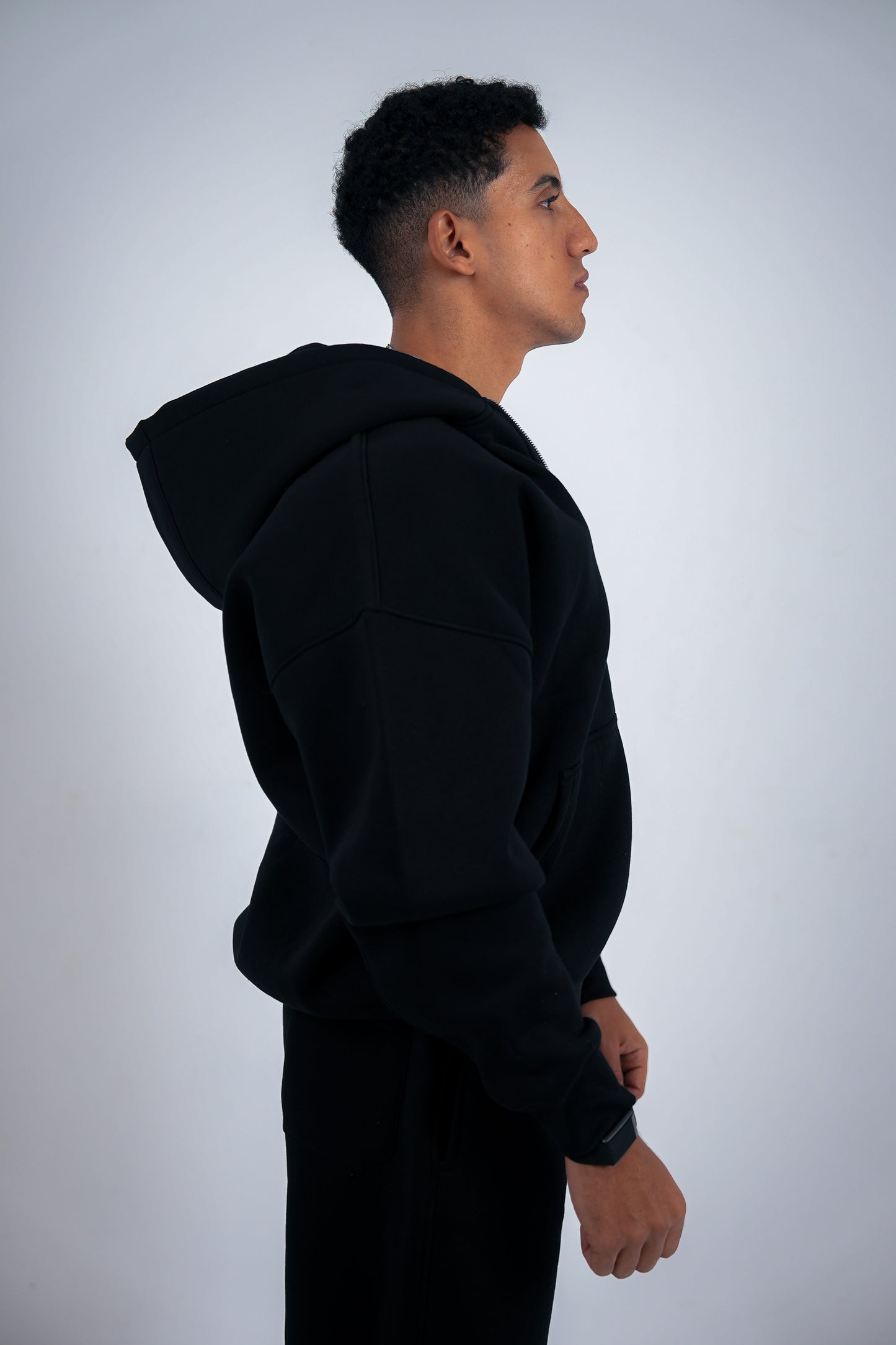 Man wearing a black RAVIX hoodie zipper against a light gray background