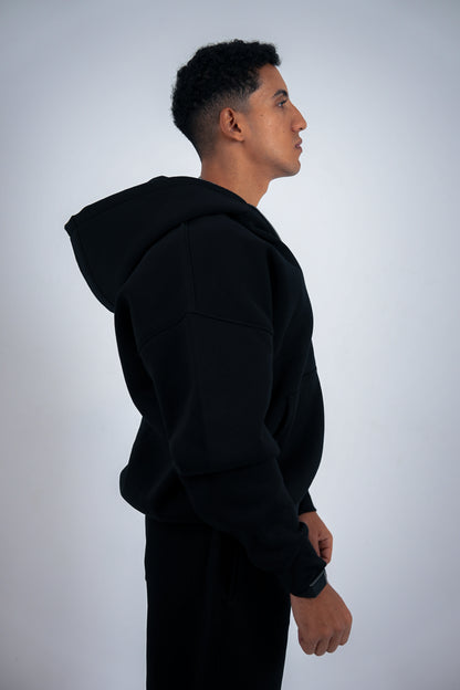 Man wearing a black RAVIX hoodie zipper against a light gray background