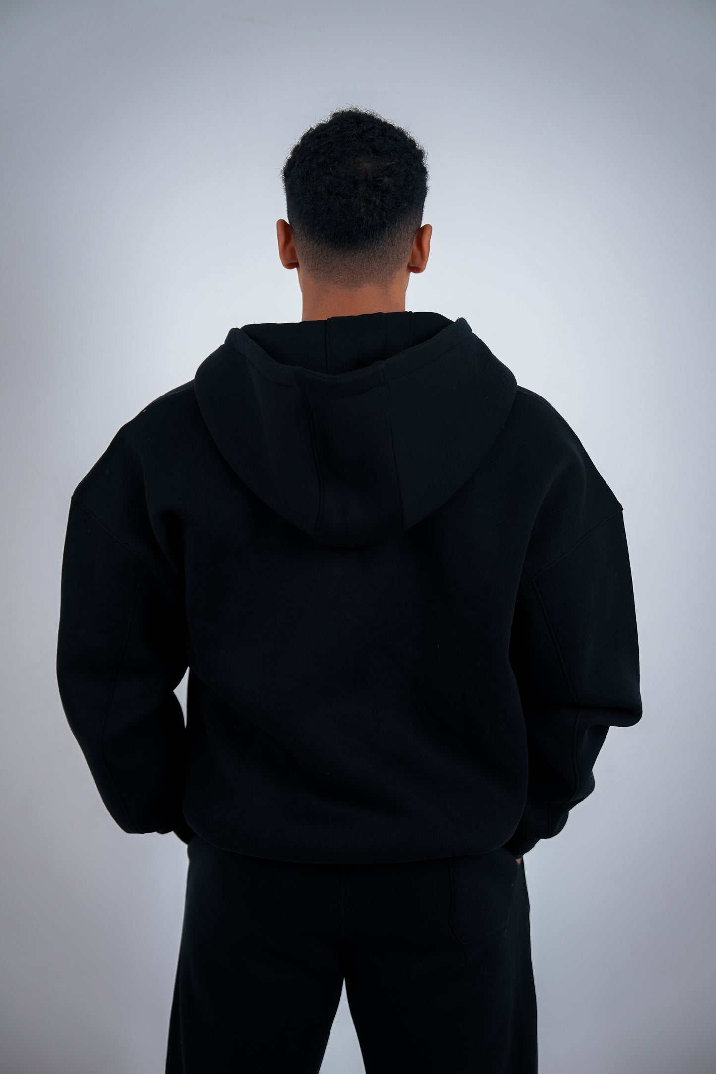 Person wearing a black RAVIX zipper jacket from behind on a light gray background