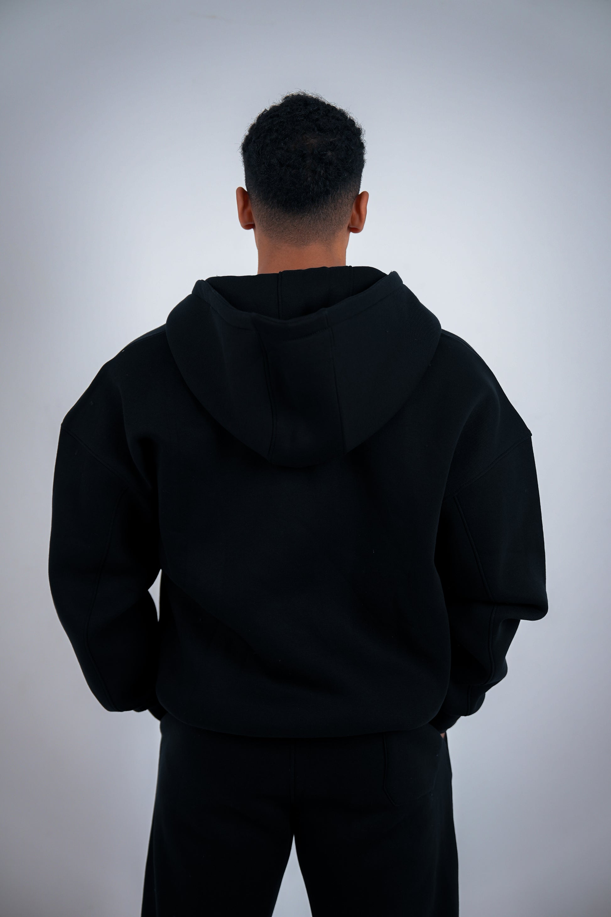 Person wearing a black RAVIX zipper jacket from behind on a light gray background
