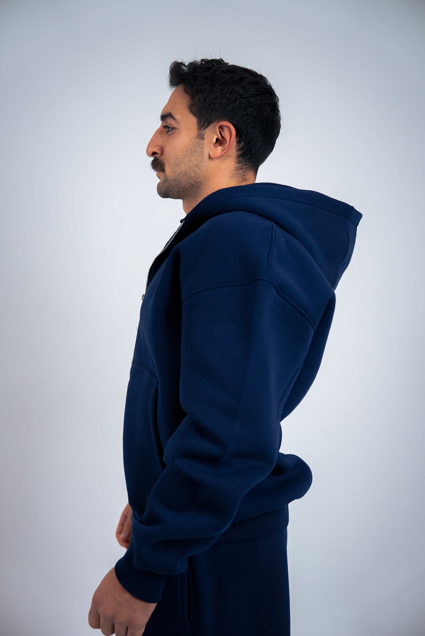 Man wearing a navy-blue RAVIX hoodie against a light gray background
