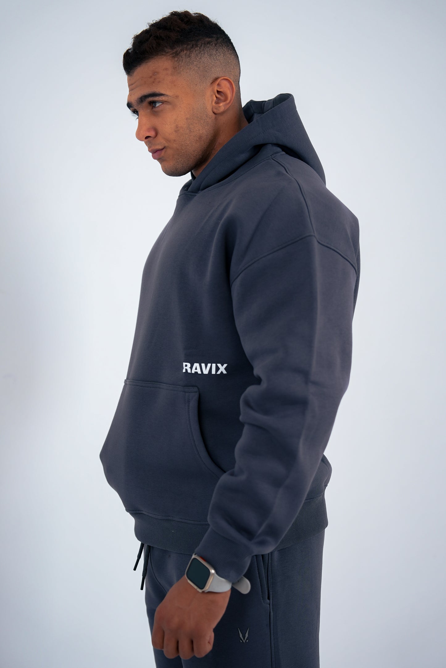 Man wearing a dark-grey hoodie with 'RAVIX' logo on a light gray background