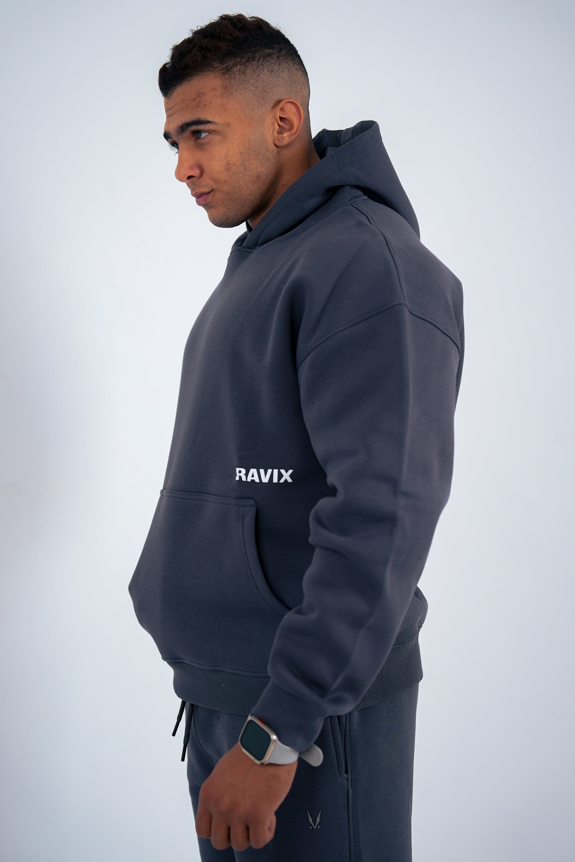 Man wearing a dark-grey hoodie with 'RAVIX' logo on a light gray background