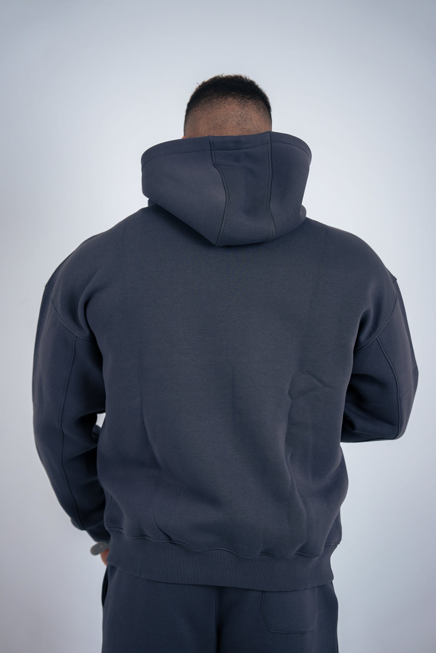 Person wearing a dark gray hoodie and pants on a light gray background