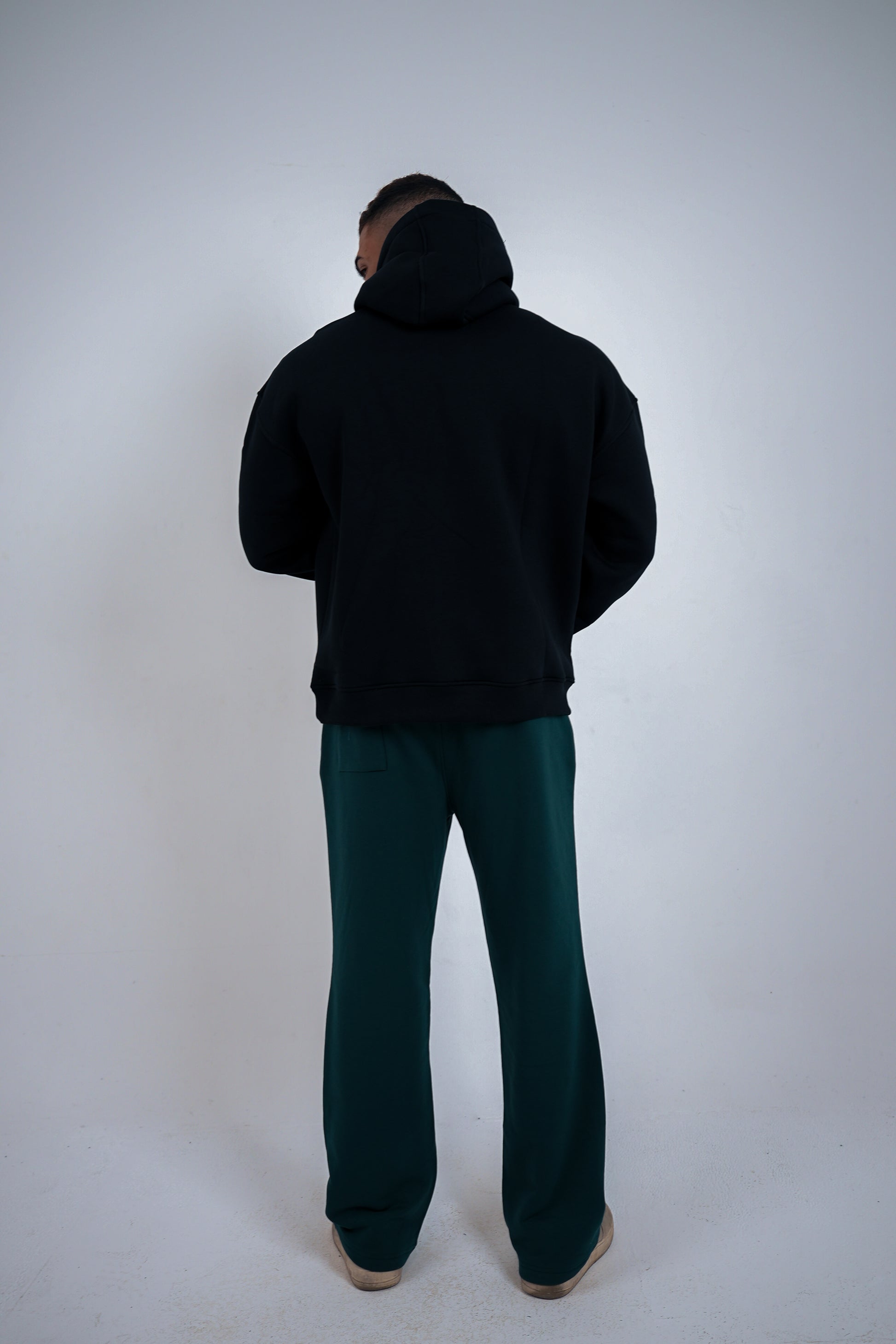 Person wearing a black hoodie and green pants on a white background