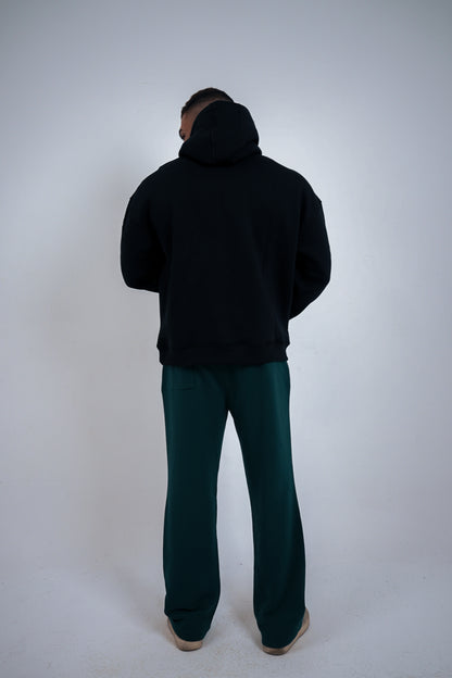 Person wearing a black hoodie and green pants on a white background