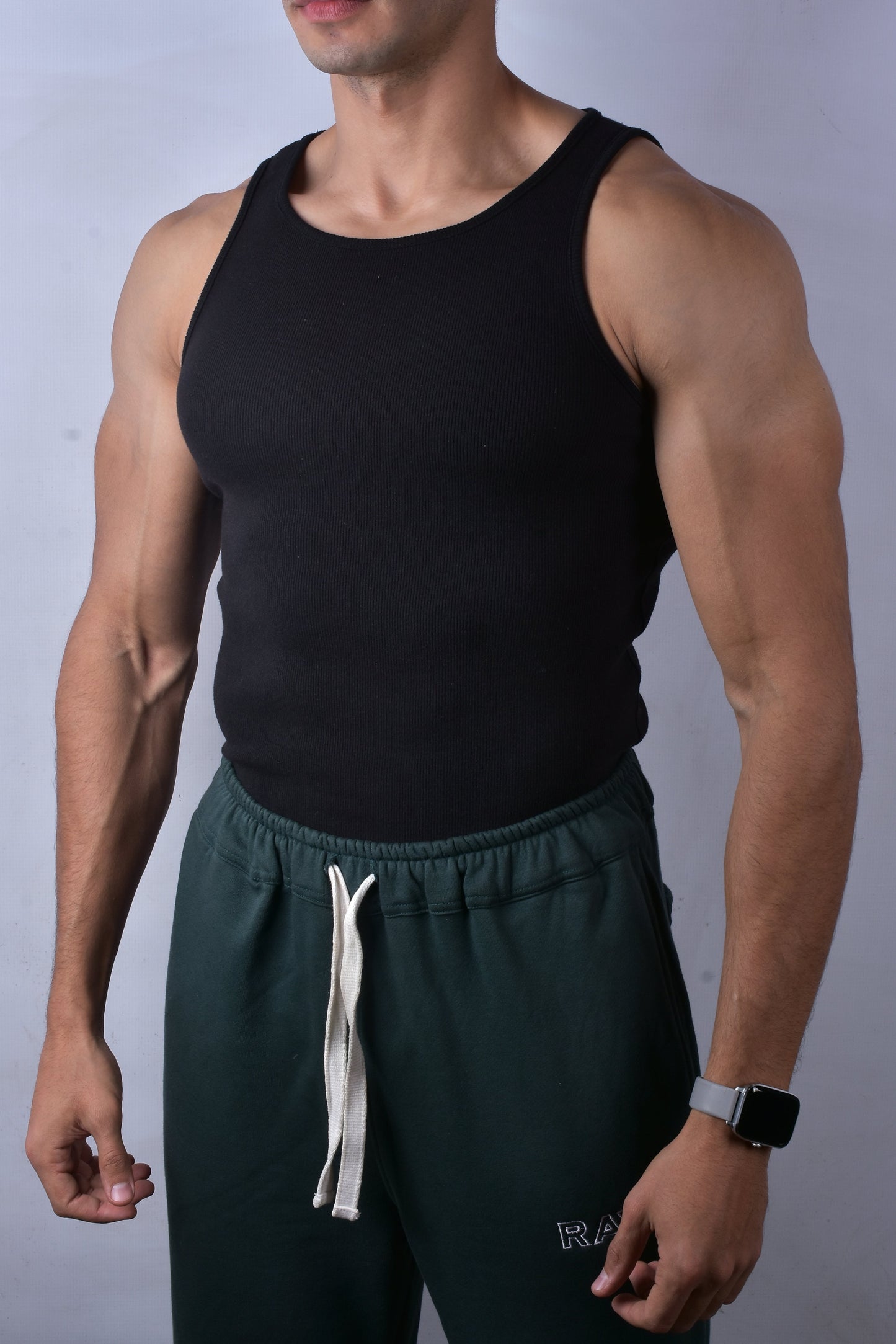 Man wearing a black tank top and green pants against a plain background
