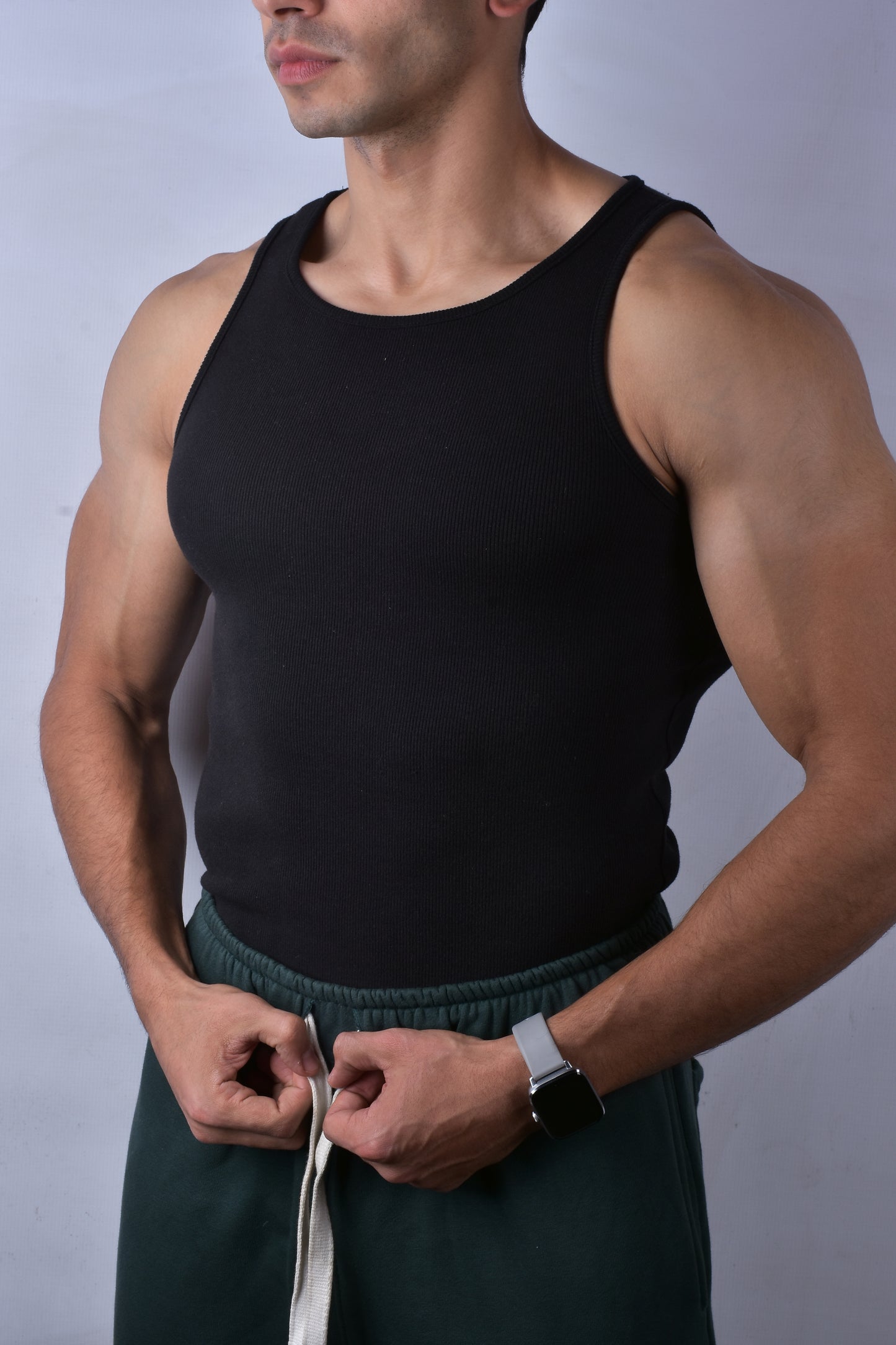 Man wearing a black tank top and green shorts against a plain background